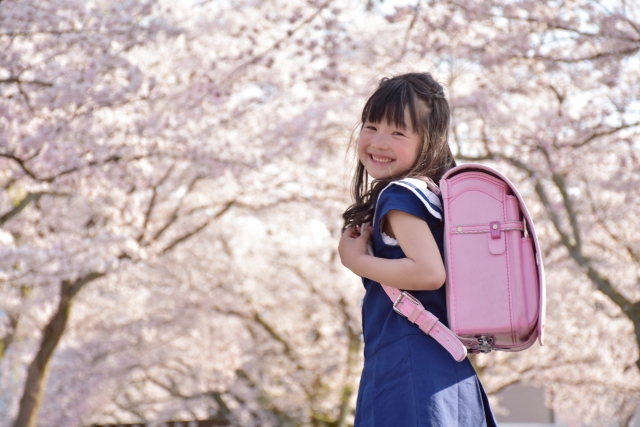 桜を背景に新しいランドセルを背負って笑顔でこちらを振り向く小学1年生の女の子