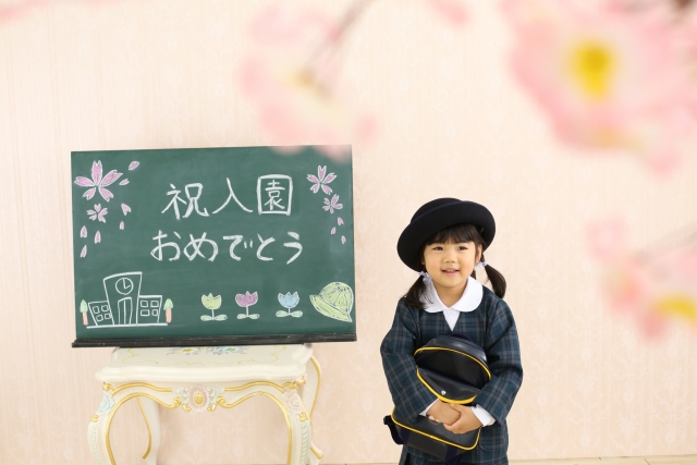「祝入園おめでとう」と書かれた黒板とリュックを抱きしめる幼稚園生の女の子