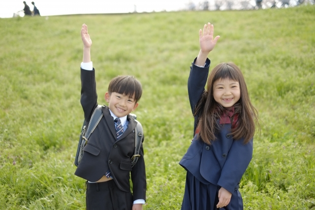 芝生に立って右手を元気よく挙げる小学1年生の男の子と女の子